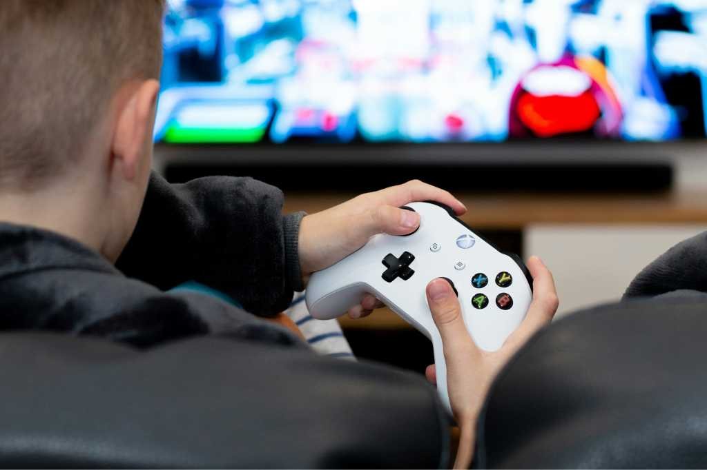 Man holding Xbox controller while playing games on TV